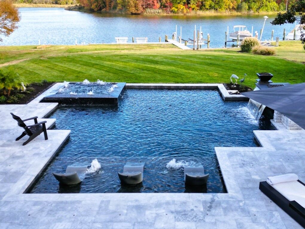 geometric pool near lake featuring spillover spa, tanning ledge, and water features