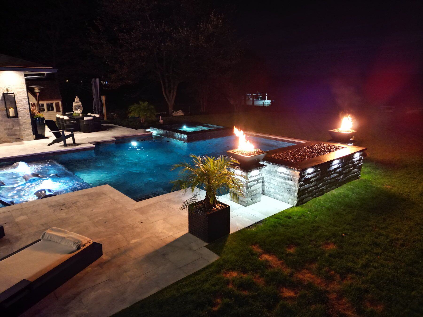 Geometric pool with spillover spa, tanning ledge, fire features, waterfall at night