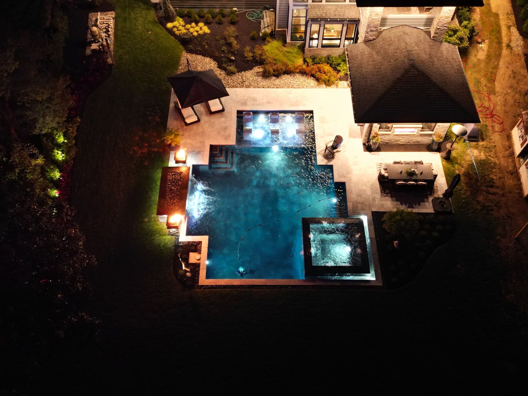 Geometric pool with spillover spa, tanning ledge, fire features, waterfall at night aerial view