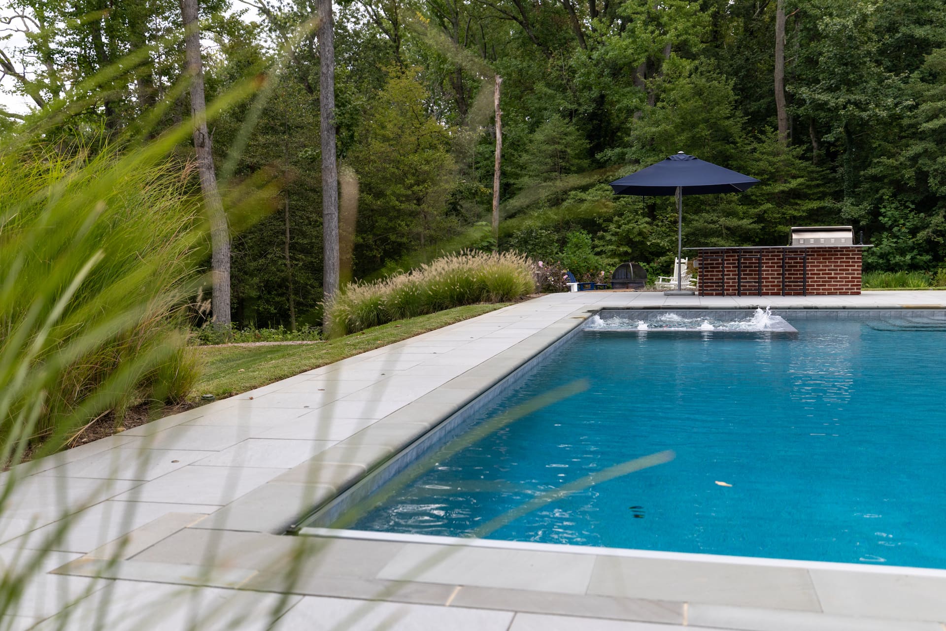 side view of pool, attached spa, outdoor kitchen, and fire pit
