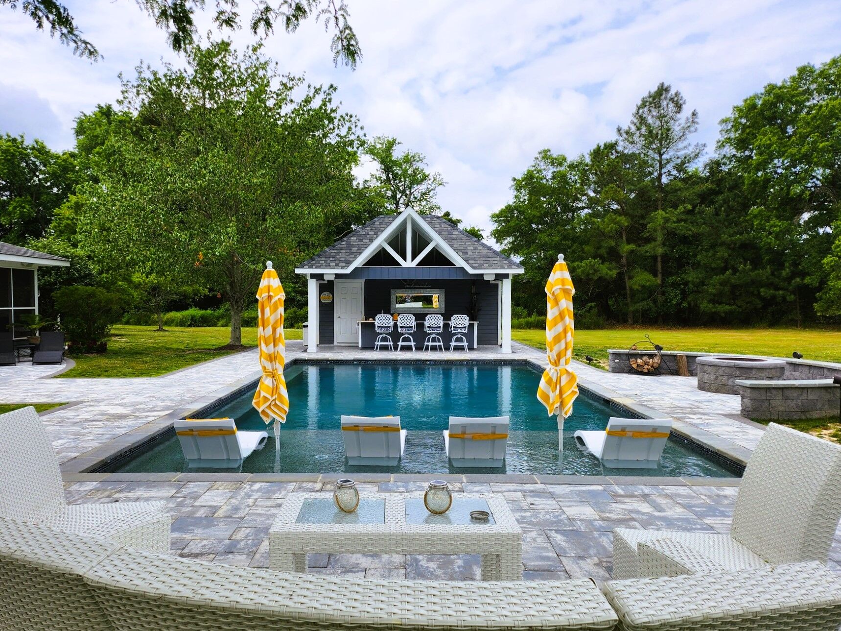geometric pool with tanning ledge surrounded by outdoor seating area, fire pit area, and outdoor bar
