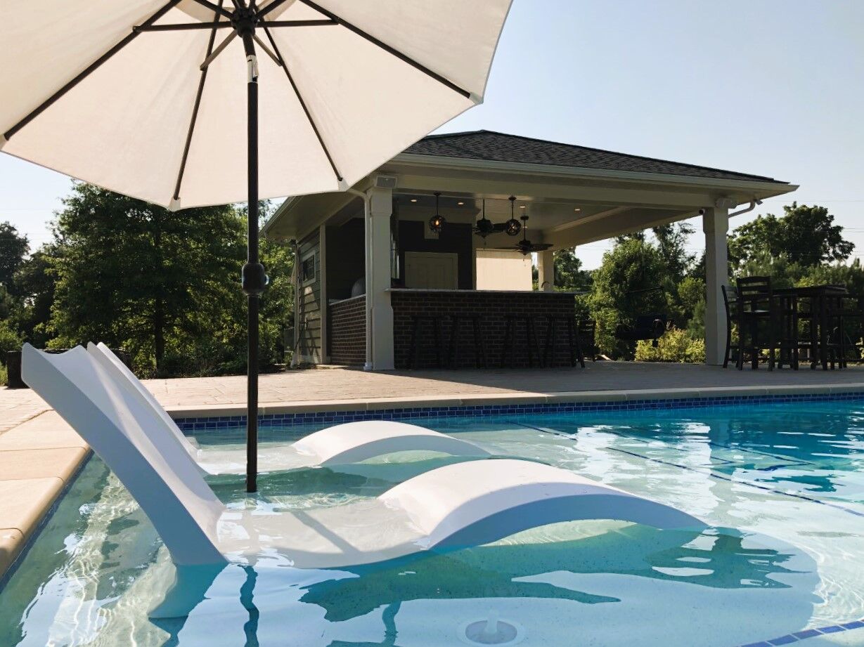 beautiful geometric pool with tanning ledge in foreground and outdoor kitchen in background