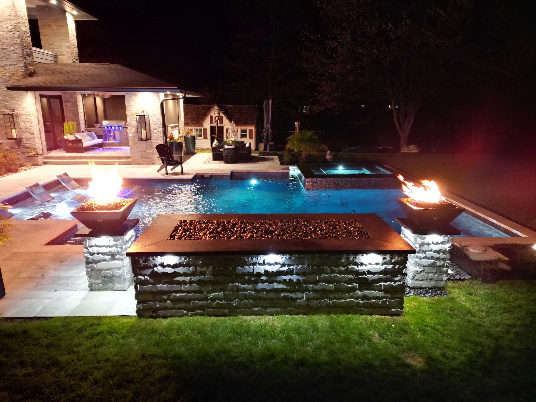 Geometric pool with spillover spa, tanning ledge, fire features, waterfall at night