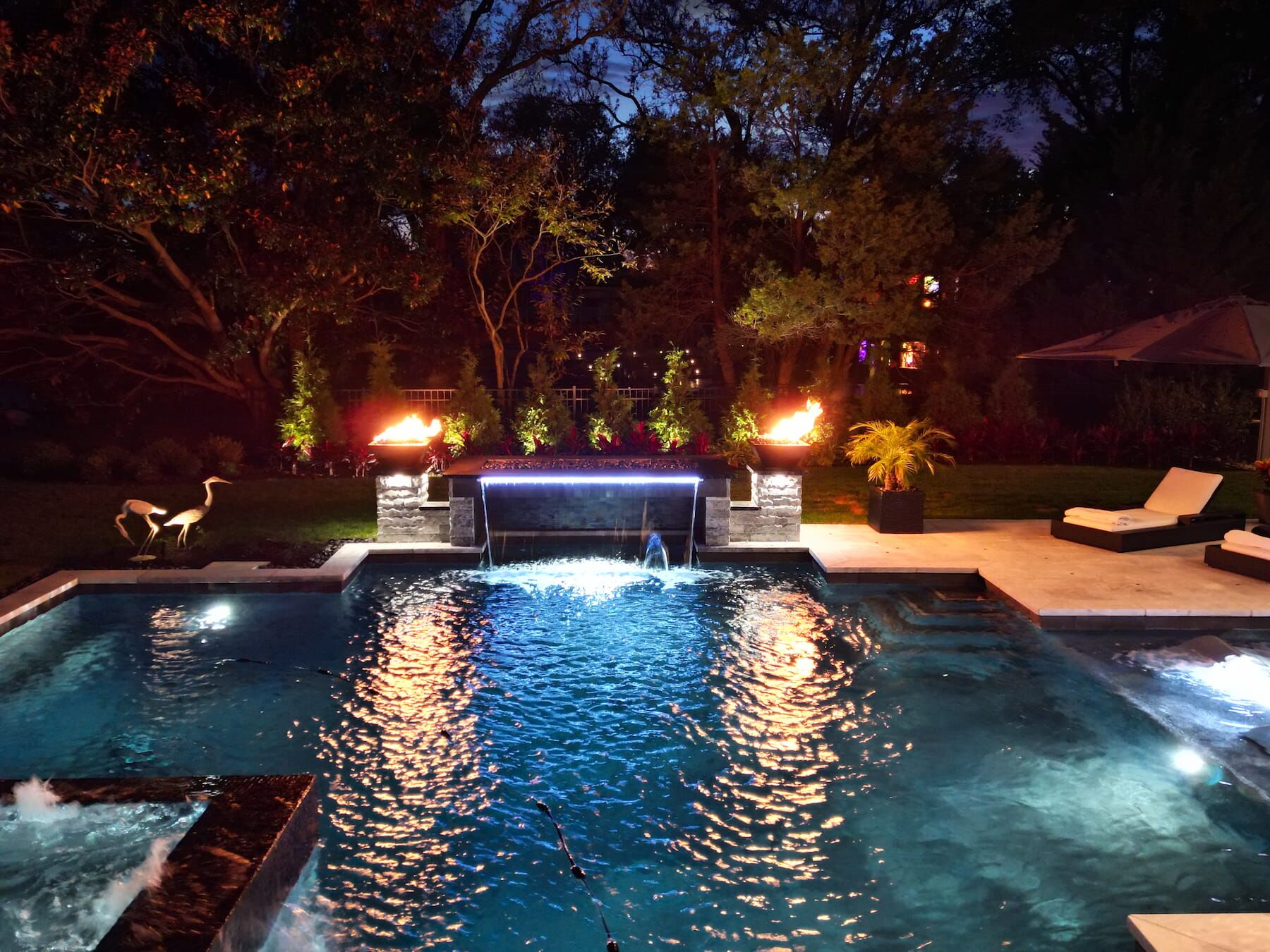 Geometric pool with fire features and waterfall at night