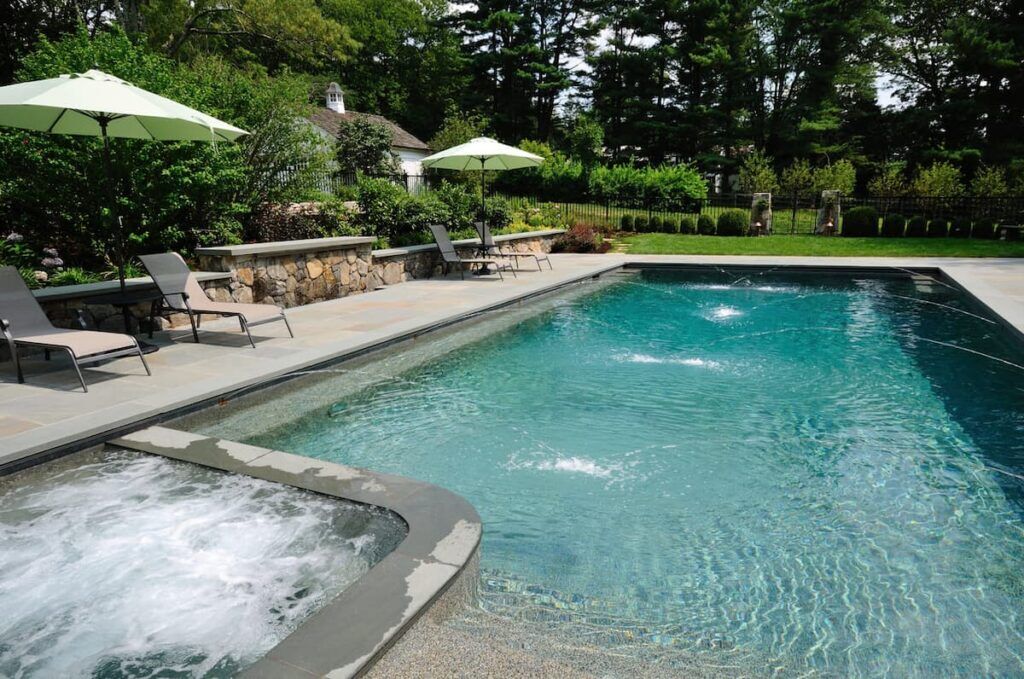 Modern backyard with a zero entry pool, integrated spa, and surrounding lounge chairs under green umbrellas.