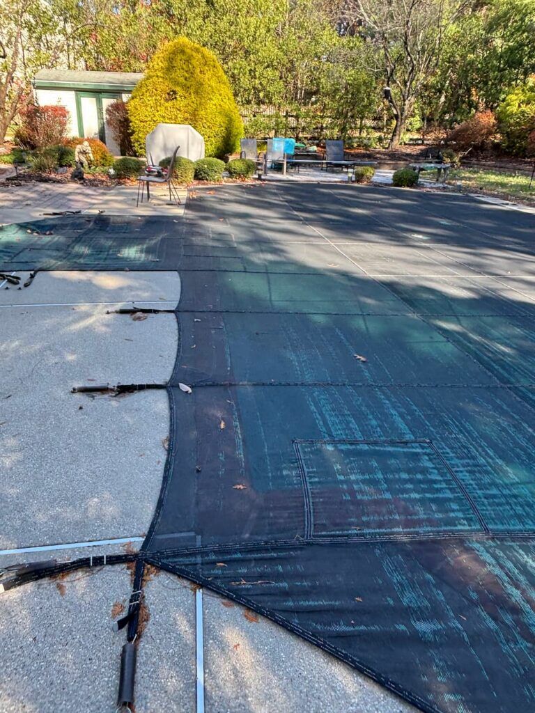 Pool covered with worn green mesh safety cover in autumn yard
